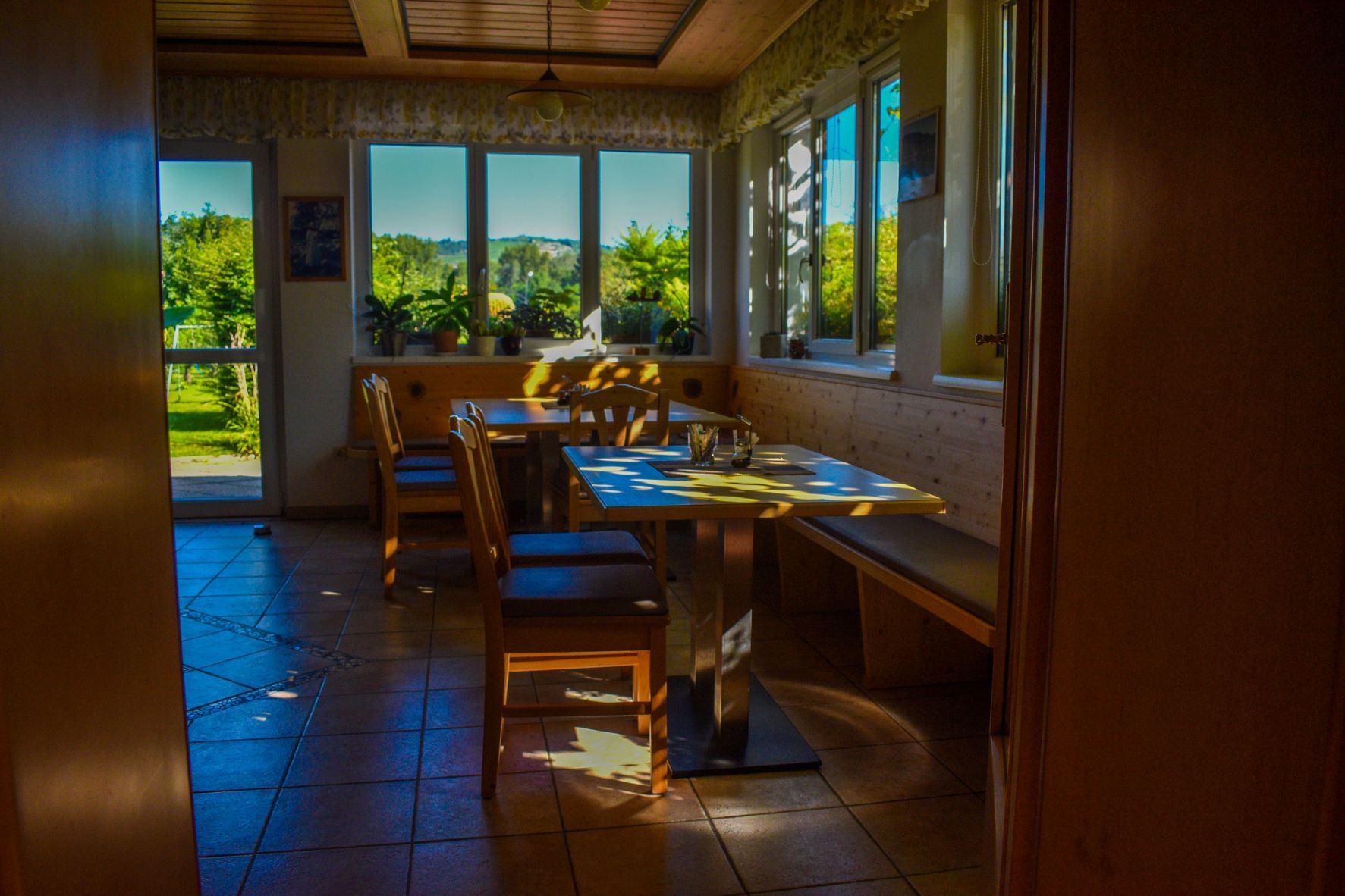 Hangulatos reggelizőterem, fabútorokkal és nagy ablakokkal, amelyek beengedik a napfényt.