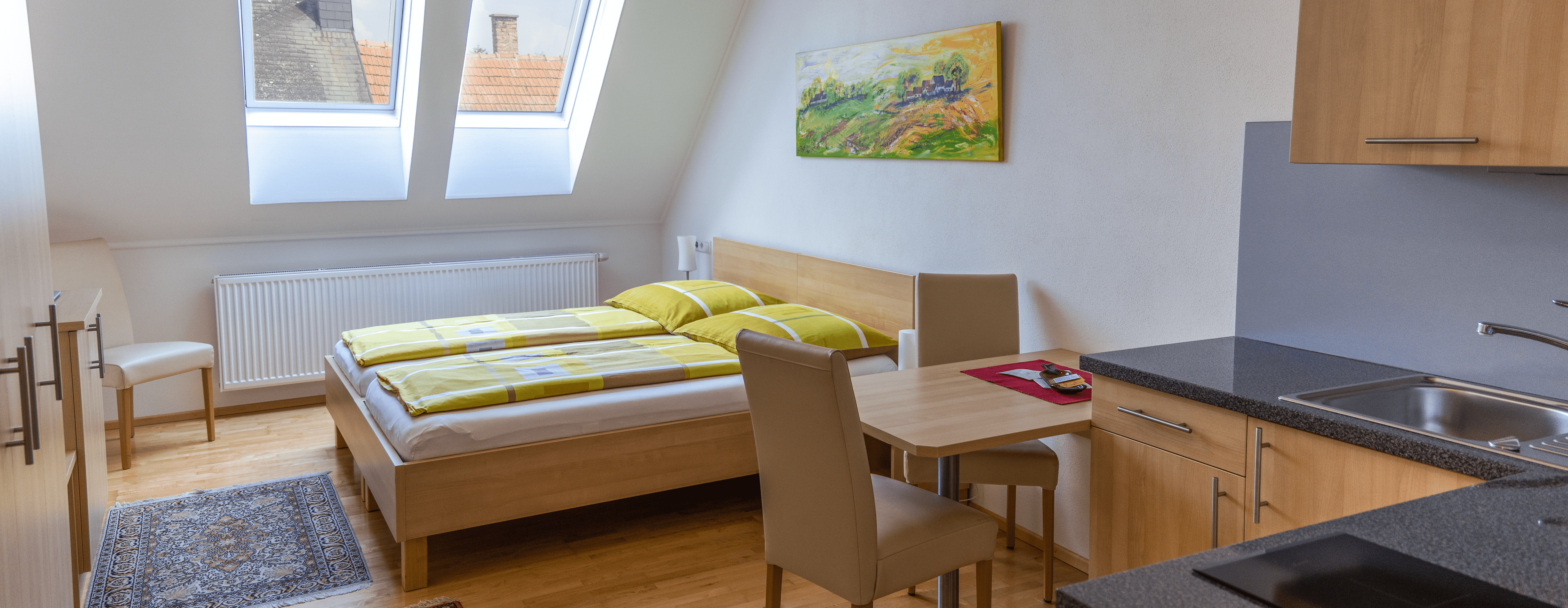 Kétágyas szoba konyhasarokkal, ággyal, asztallal és székekkel.