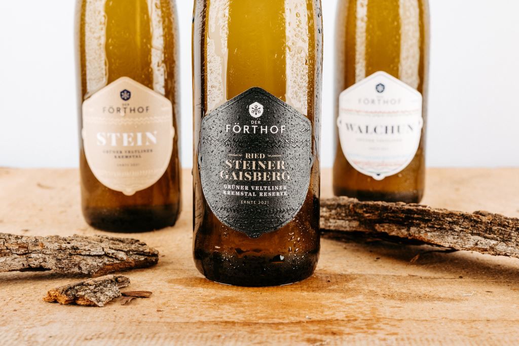 Három Förthof borosüveg egy fából készült asztalon, kéregdarabokkal.