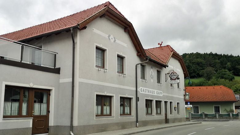 Gasthaus Gapp Weinburgban, szürke homlokzattal és piros tetővel.