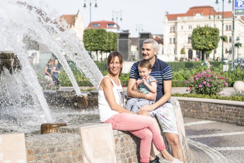 Egy mosolygó család ül egy szökőkút mellett Tulln főterén.