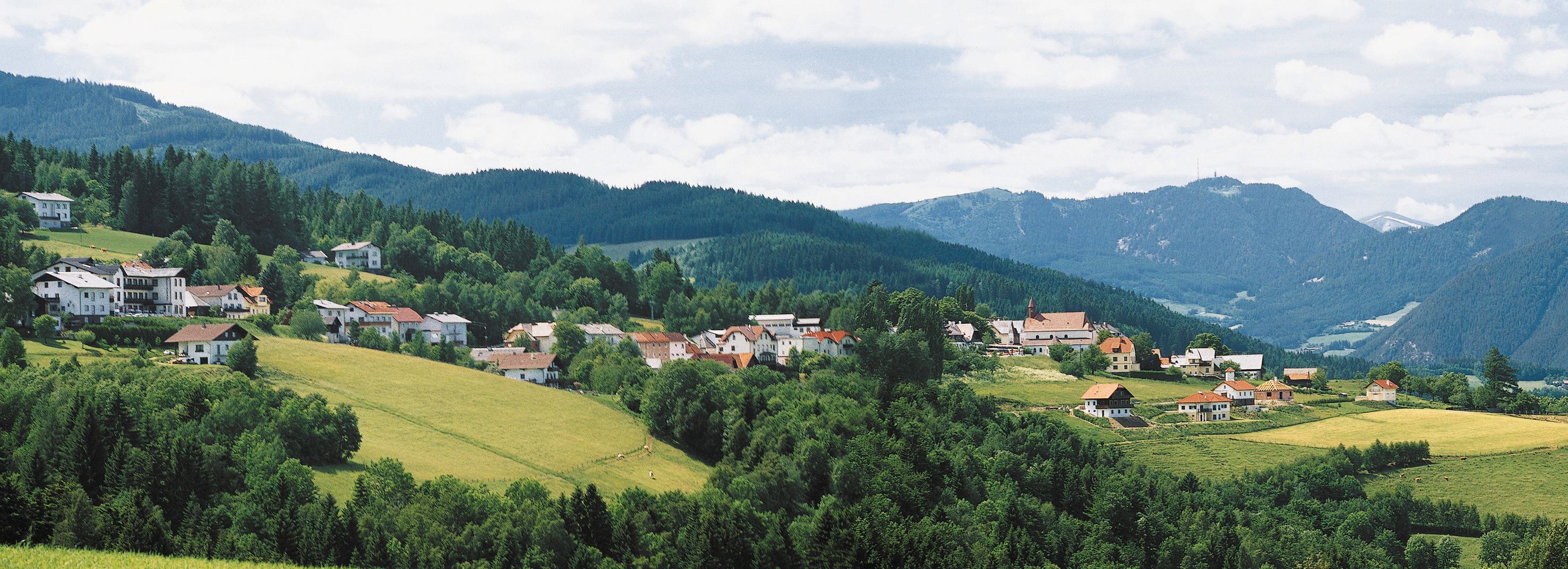 A St. Corona am Wechsel panorámája zöld dombokkal és hegyekkel a háttérben.