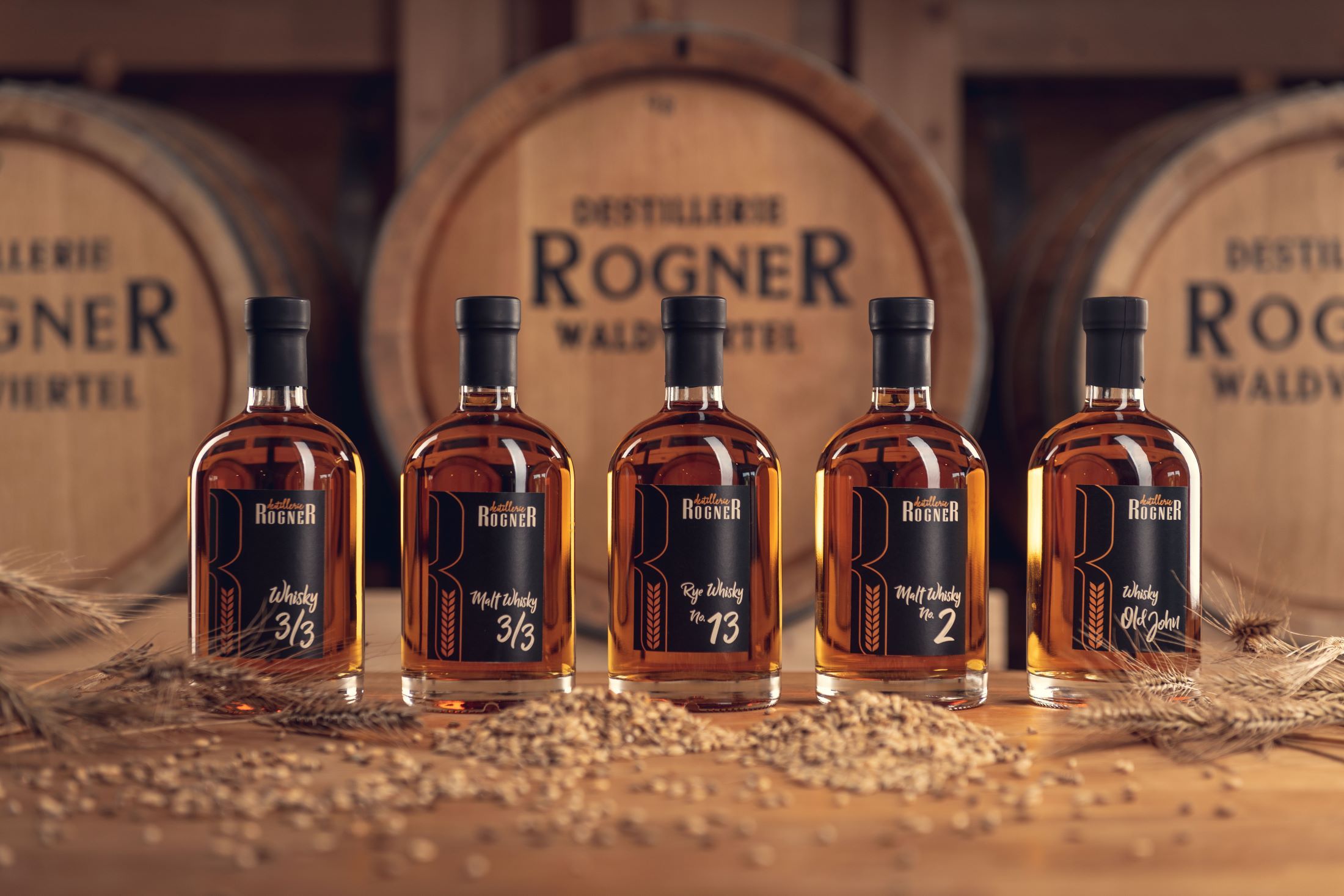 Öt üveg whisky a Rogner lepárlóból a fahordók előtt.