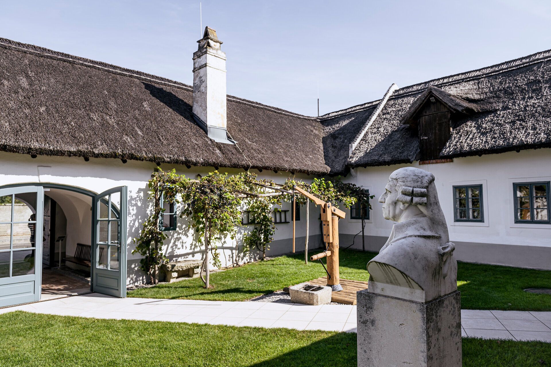 Haydn szülőházának belső udvara nádtetővel és Haydn mellszobrával.
