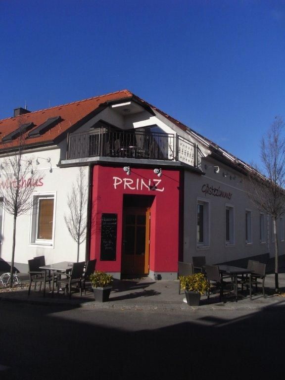 Egy "Prinz" feliratú épület külső nézete, vendégkert asztalokkal és székekkel, kék égbolt.