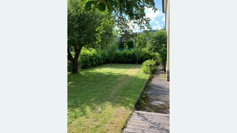 Gondozott kert gyeppel, fákkal és bokrokkal egy ház mellett.