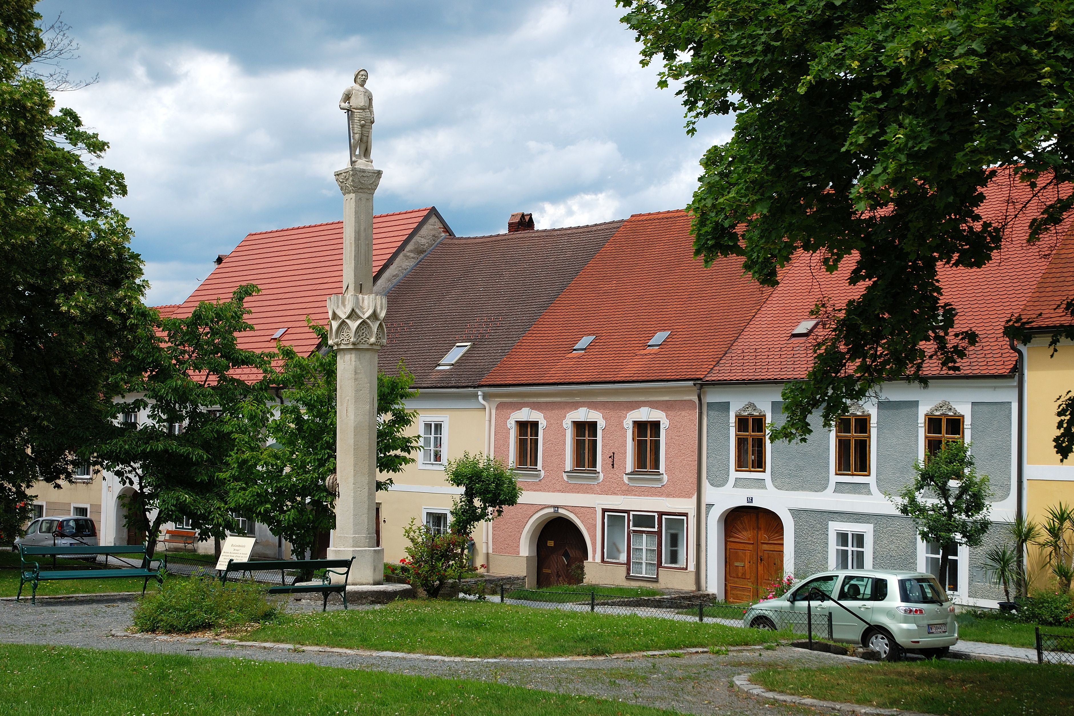 Szobor egy oszlopon a színes házak előtt Drosendorf-Zissersdorfban.
