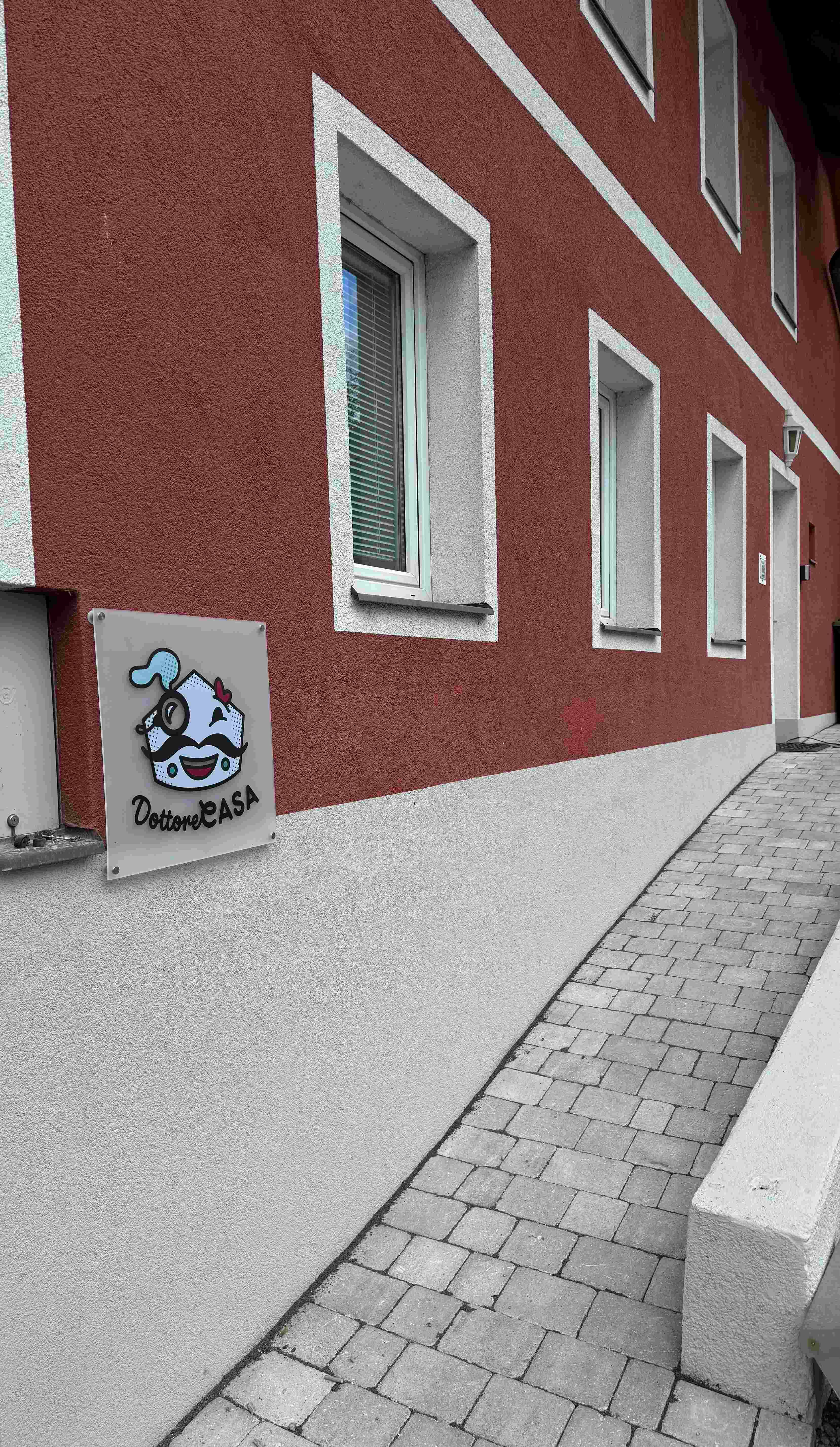 Egy piros homlokzatú épület külső nézete, "Dottore Casa" feliratú táblával.