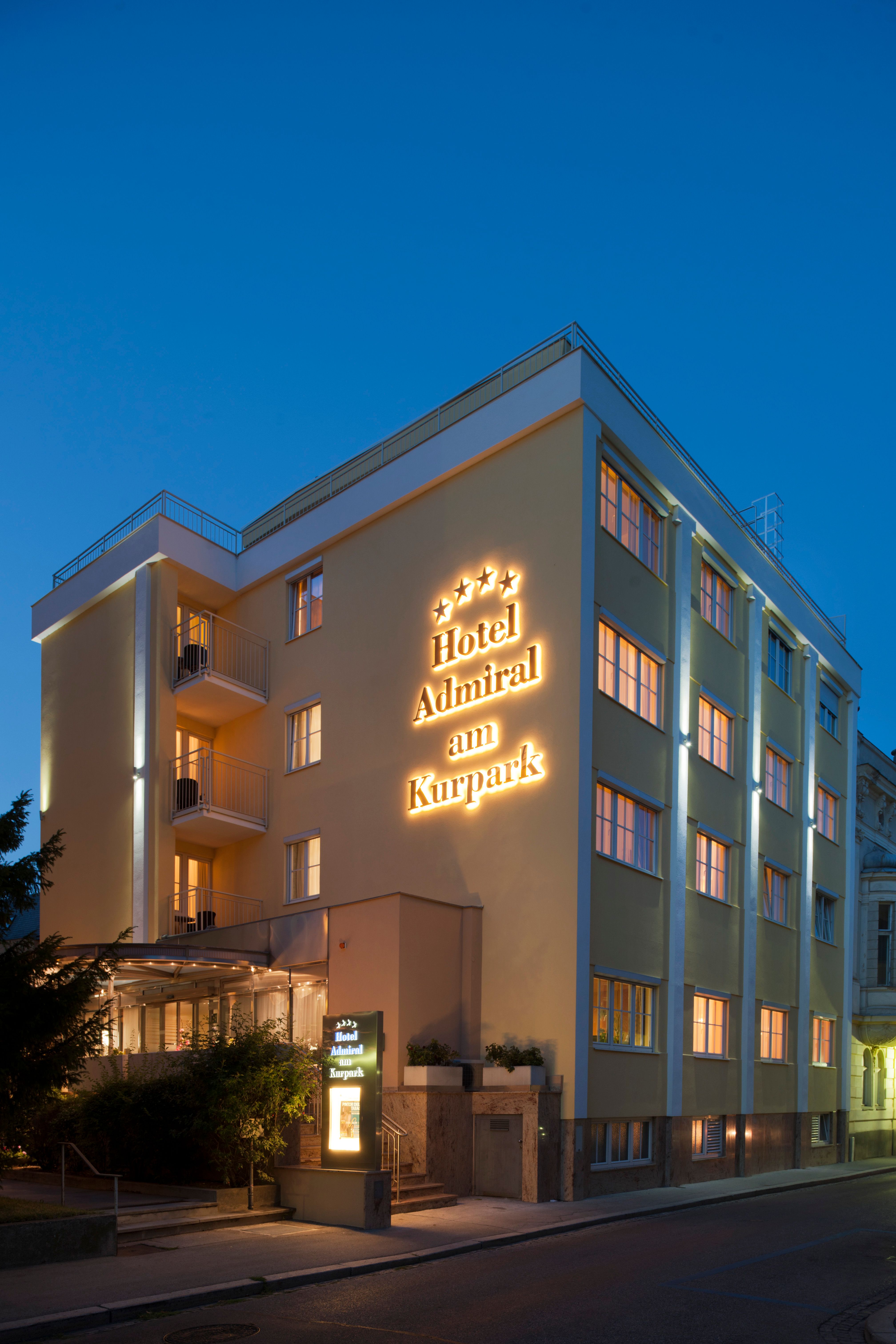 Egy szálloda külső nézete alkonyatkor, "Hotel Admiral am Kurpark" felirattal.