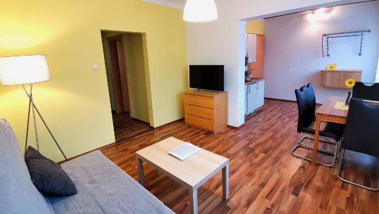 Modern nappali fapadlóval, kanapéval, asztallal, TV-vel és étkezővel.