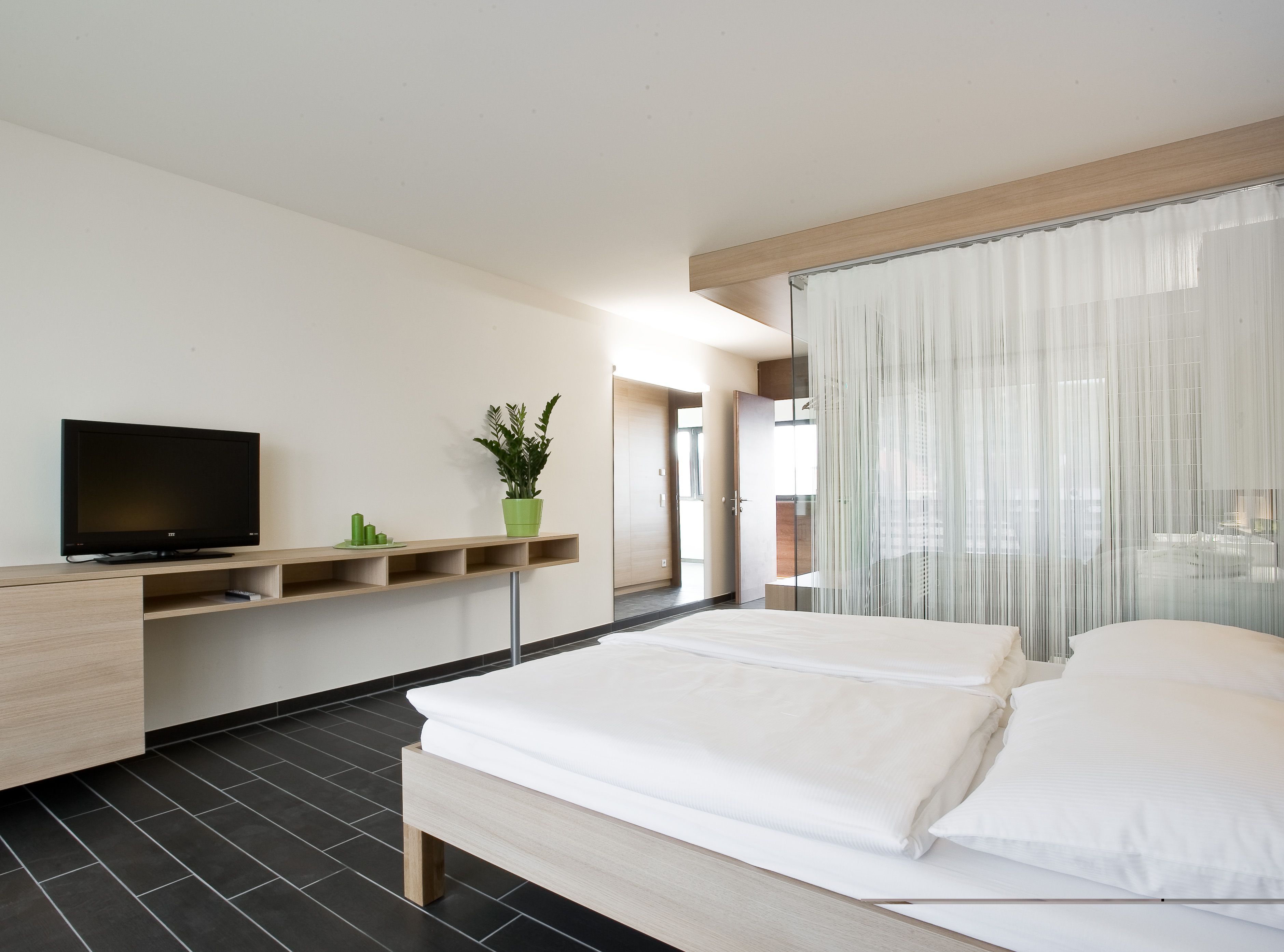 Modern szállodai szoba franciaággyal, televízióval és növényekkel.