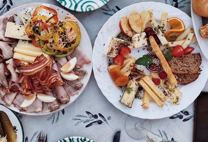 Két tányér felvágottal, sajttal, zöldséggel és gyümölccsel az asztalon.