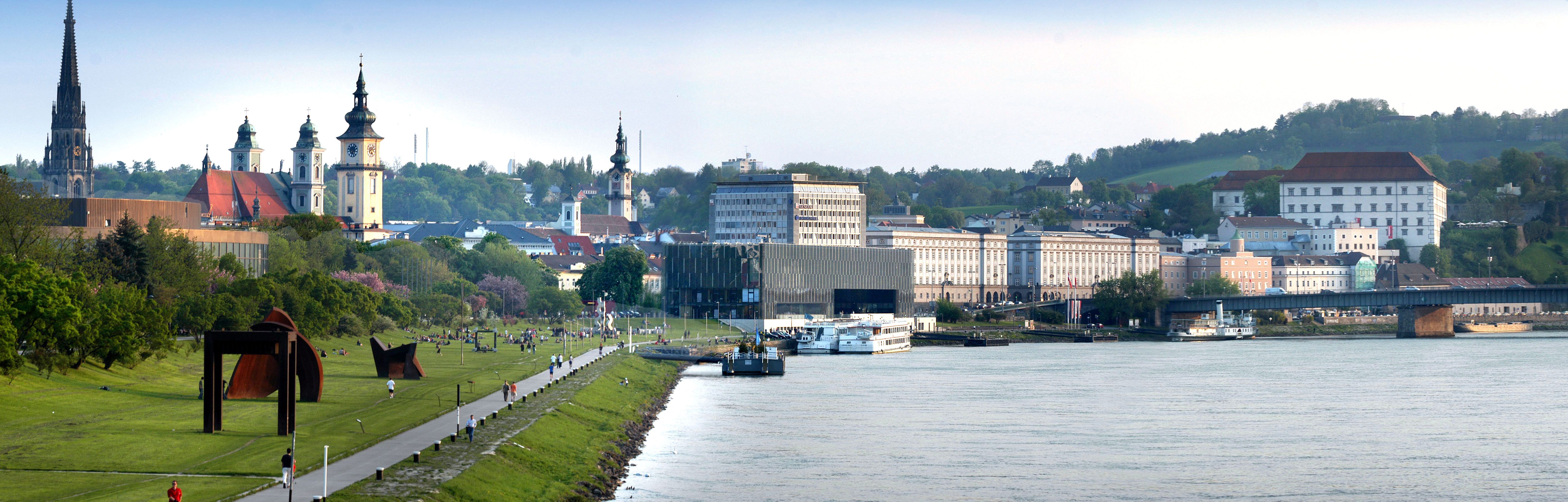 Linz panorámája a Dunával, templomokkal és modern építészettel.