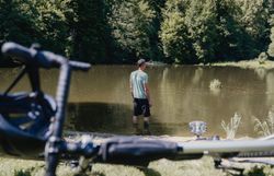 Ein Mann in Sportkleidung steht im Strandbad und blickt in die Ferne, im Vordergrund ist ein Rad angeschnitten