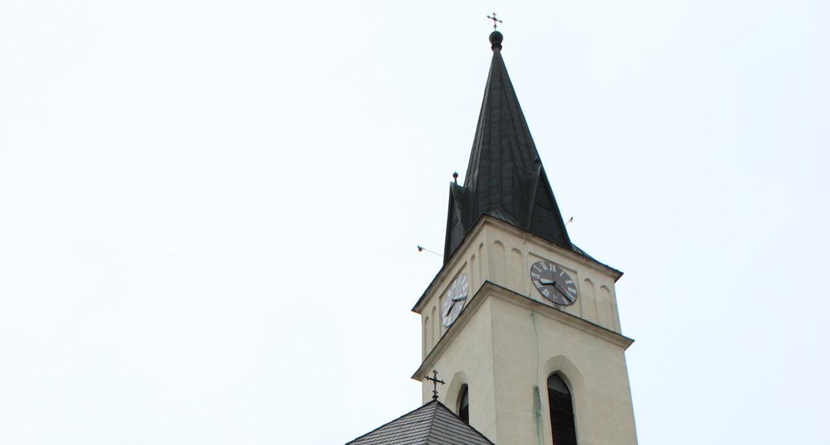Templomtorony órával és csúcsos tetővel a fényes égbolt előtt.