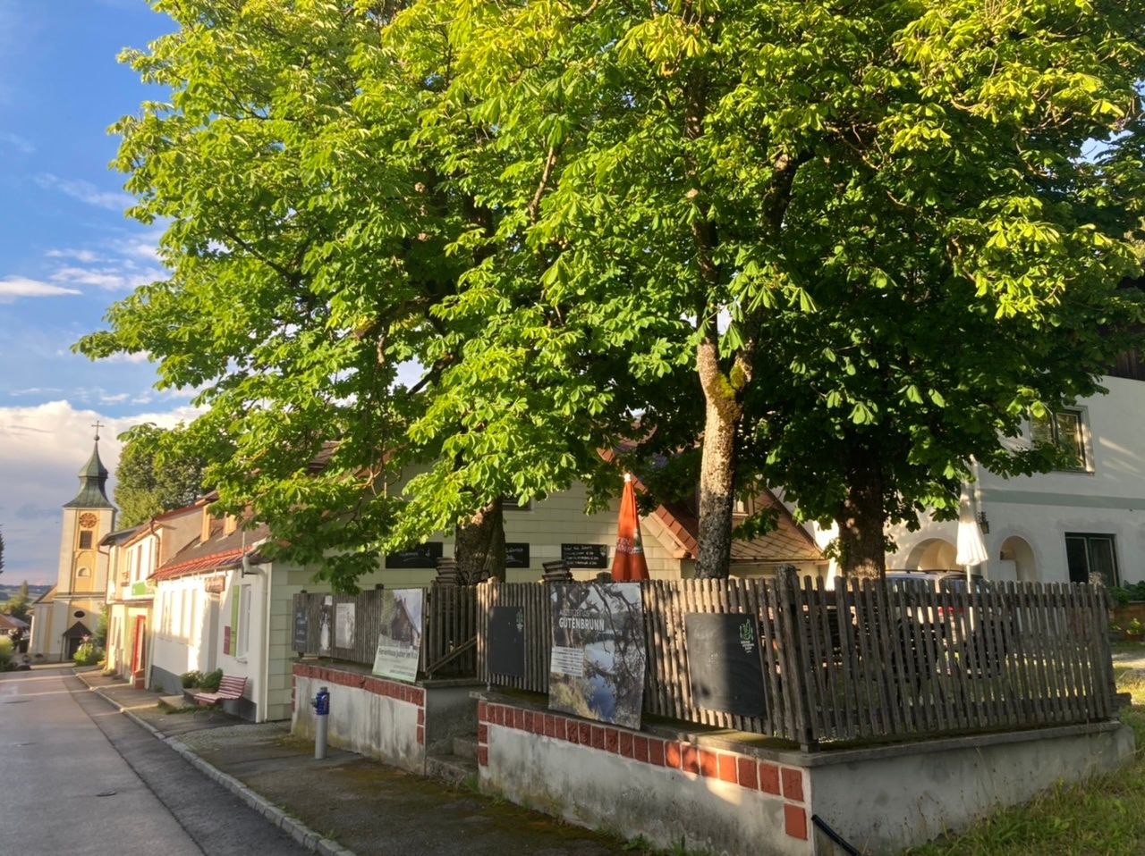 Hagyományos vendéglő gesztenyés kerttel és templommal a háttérben.
