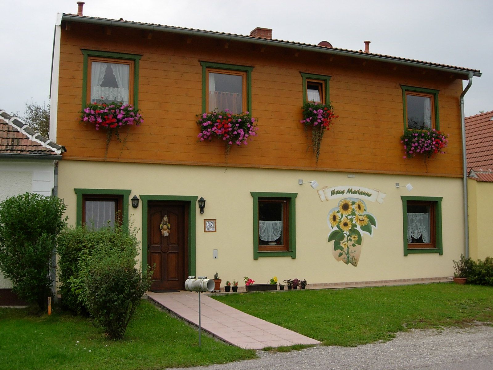 Kétemeletes ház, fa burkolattal és virágládákkal, a "Haus Marianne" felirattal.