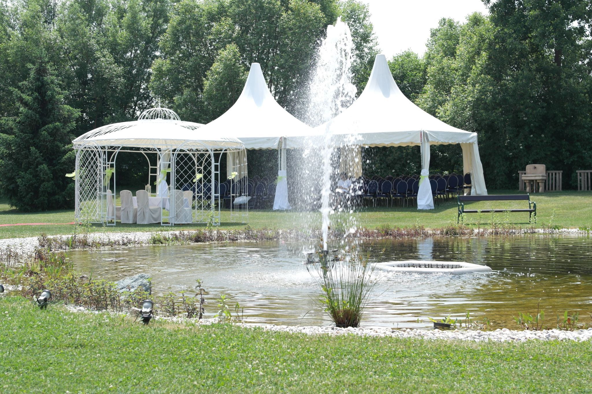 Esküvői pavilon és sátrak egy kerti szökőkutas tó mellett.
