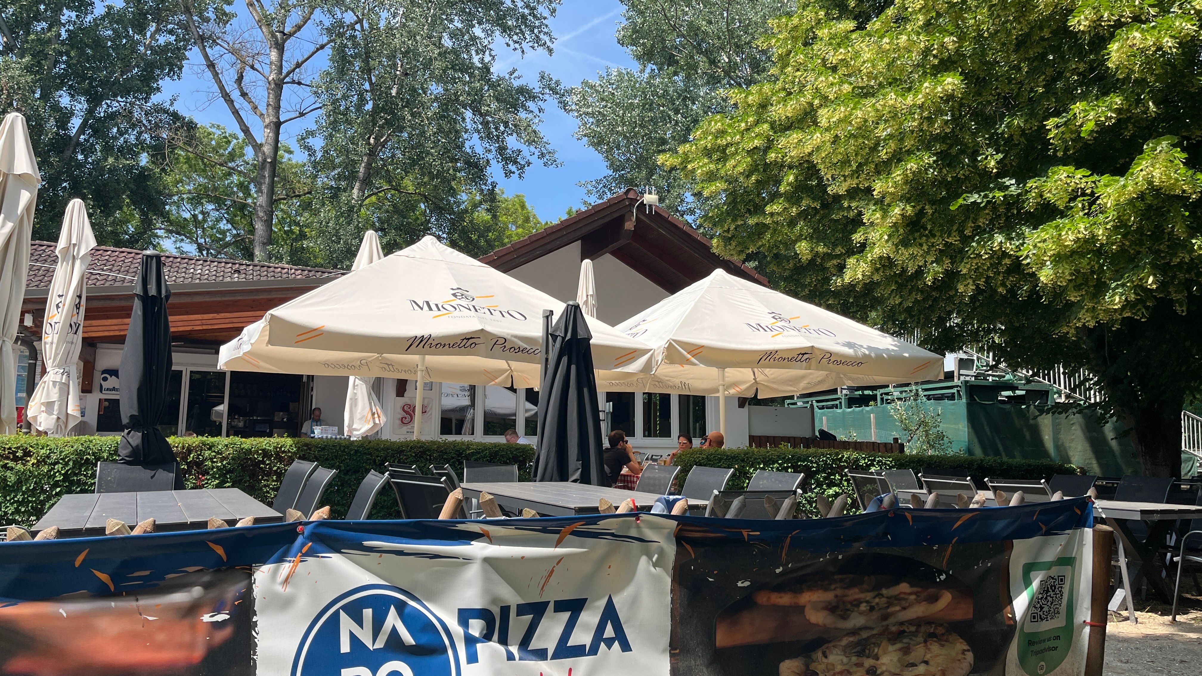 Vendégkert, kilátással a pizzéria épületére, a háttérben fák.