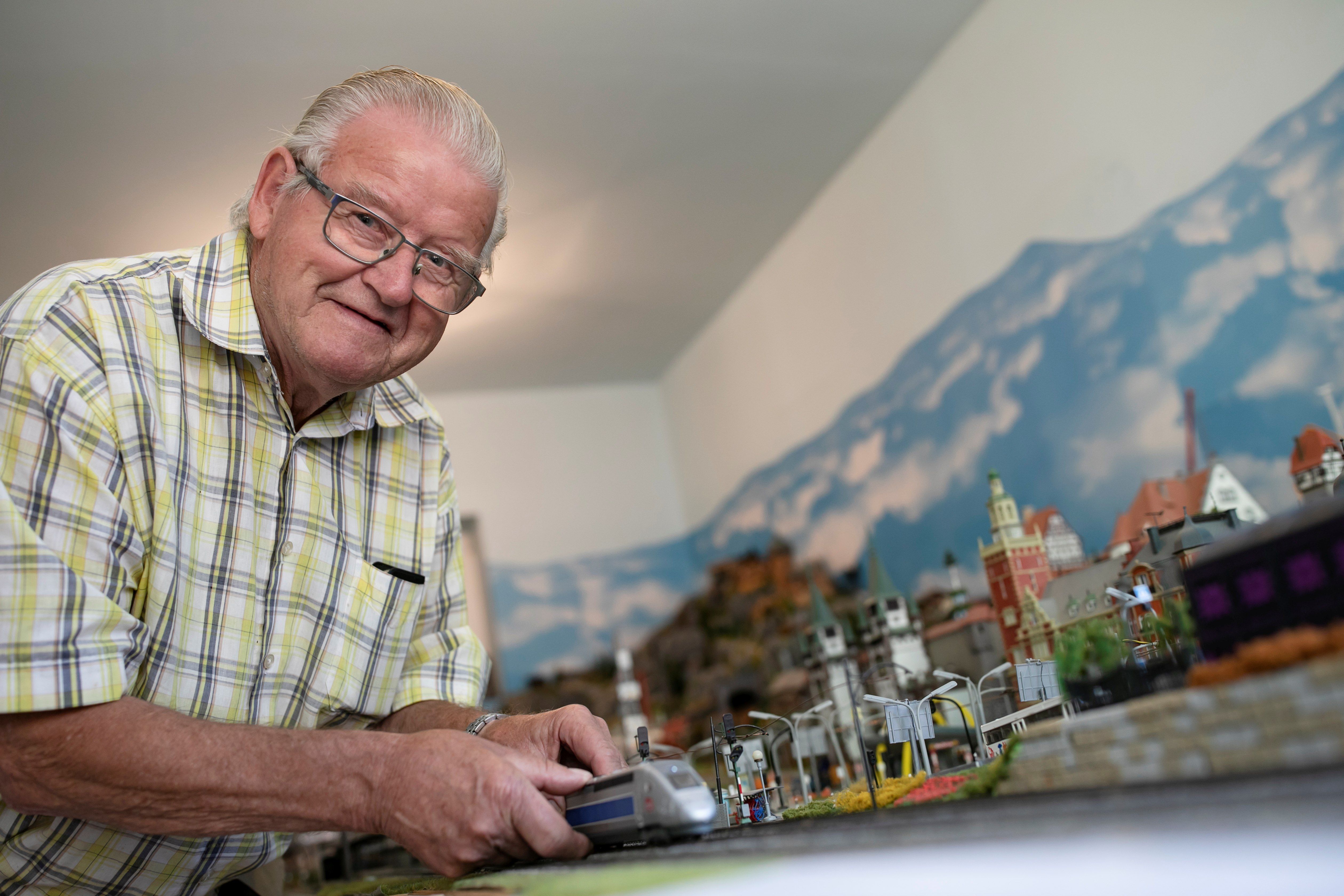 Moser nagypapa a modellvasút-makettje előtt áll, és egy mozdonyt mutat. 
