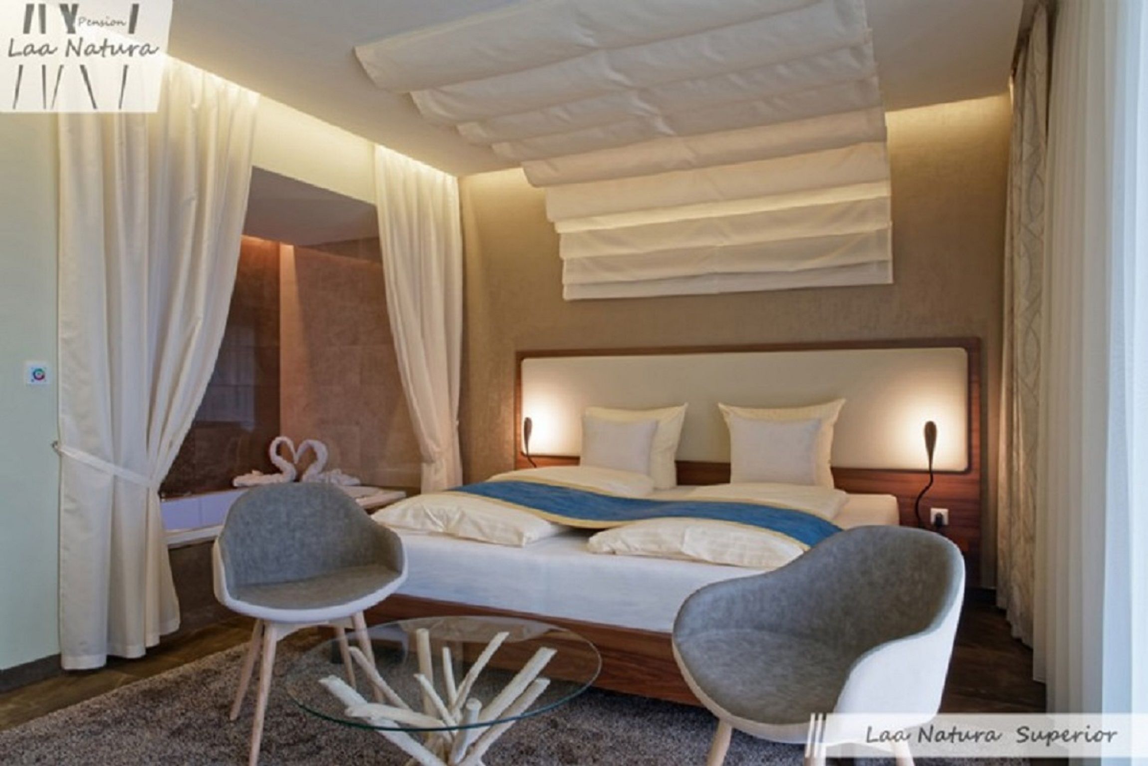 Modern kétágyas szoba nagy ággyal, két szürke székkel és üvegasztallal.