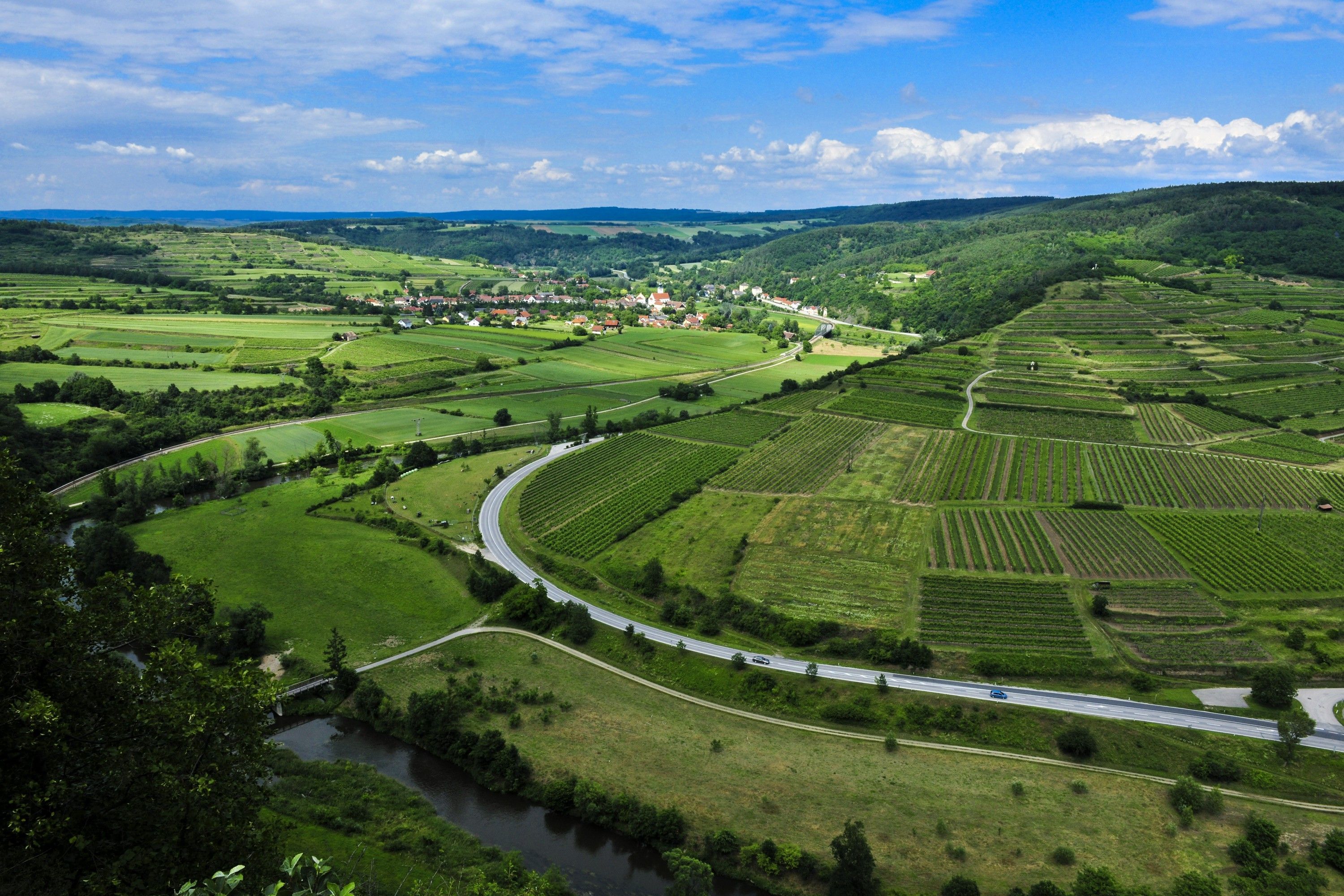 Tájkép a Kamptal Schönberg natúrparkban, mezőkkel, utakkal és egy folyóval.