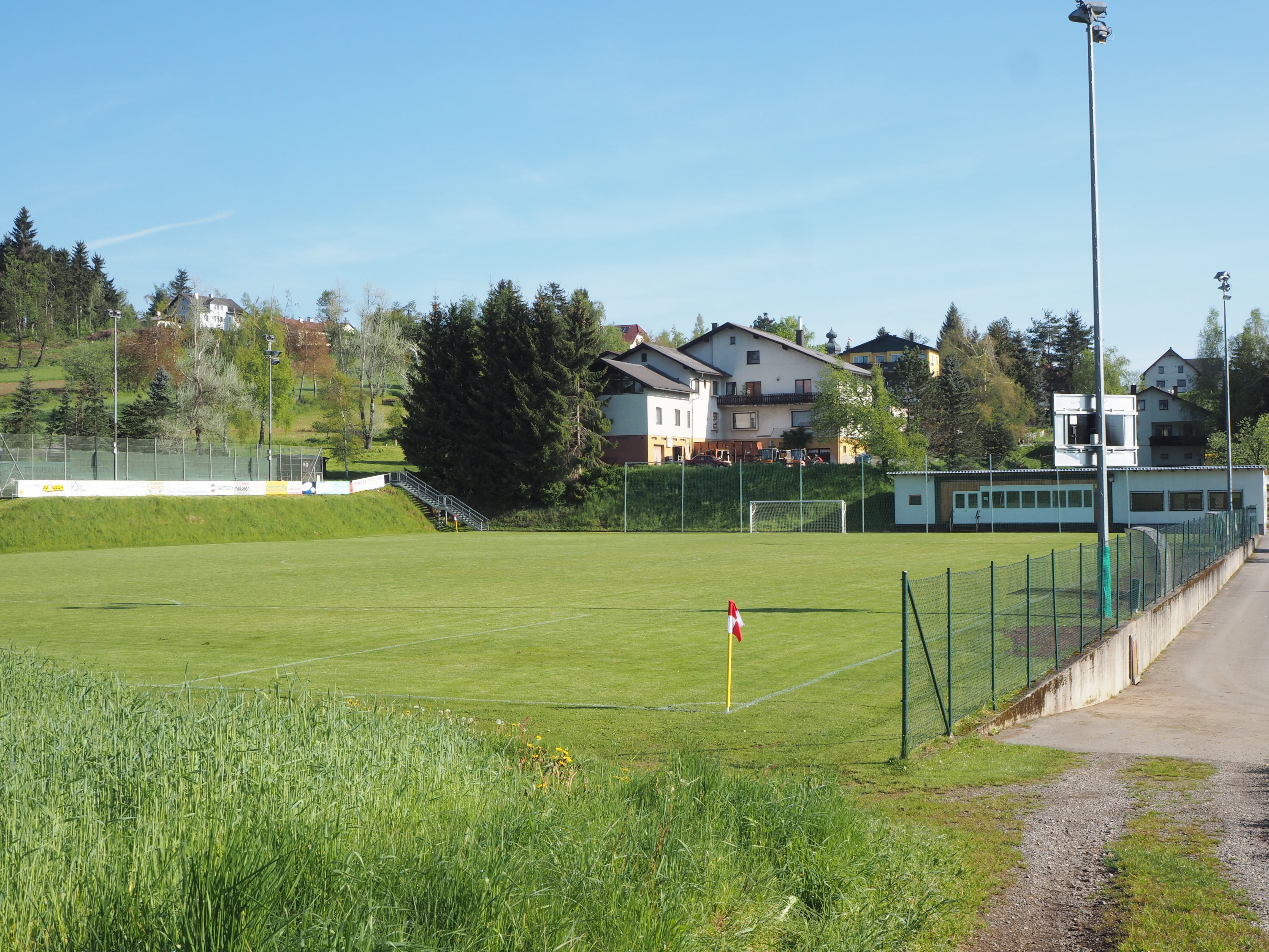 Egy üres futballpálya a környező épületekkel és fákkal egy napsütéses napon.