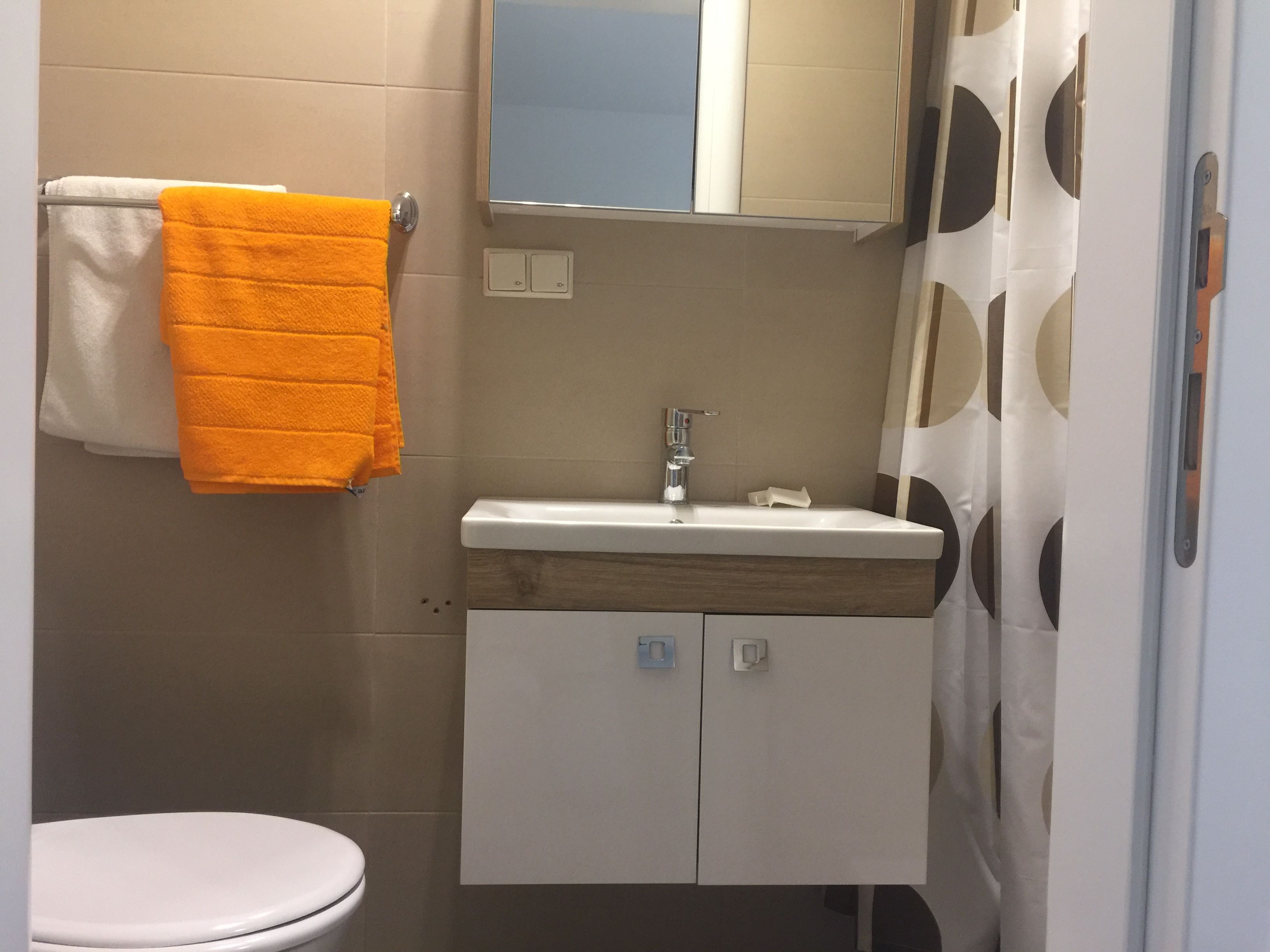 Kis fürdőszoba mosdóval, tükörrel, zuhanyfüggönnyel és törölközőkkel.