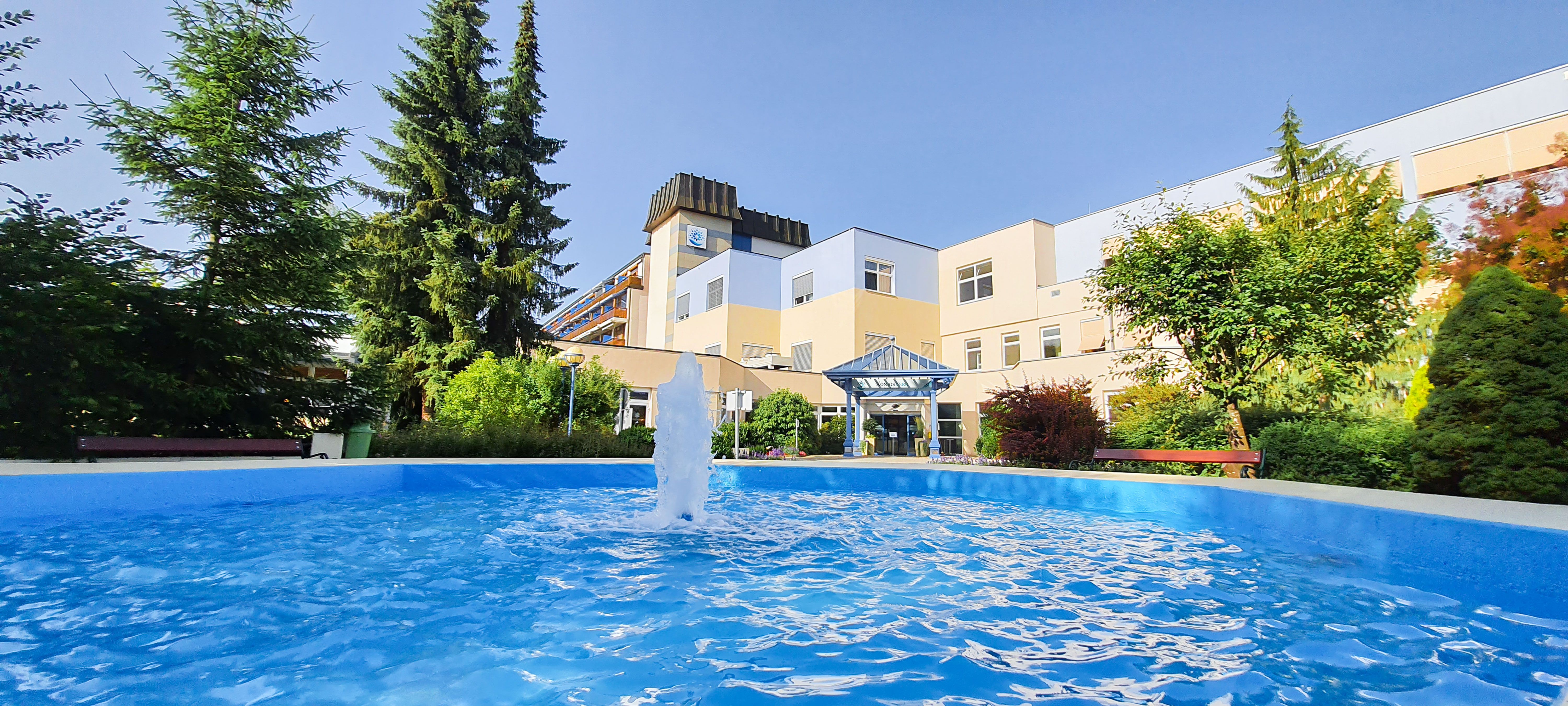 Egy gyógyfürdő külső nézete szökőkúttal és kerttel.