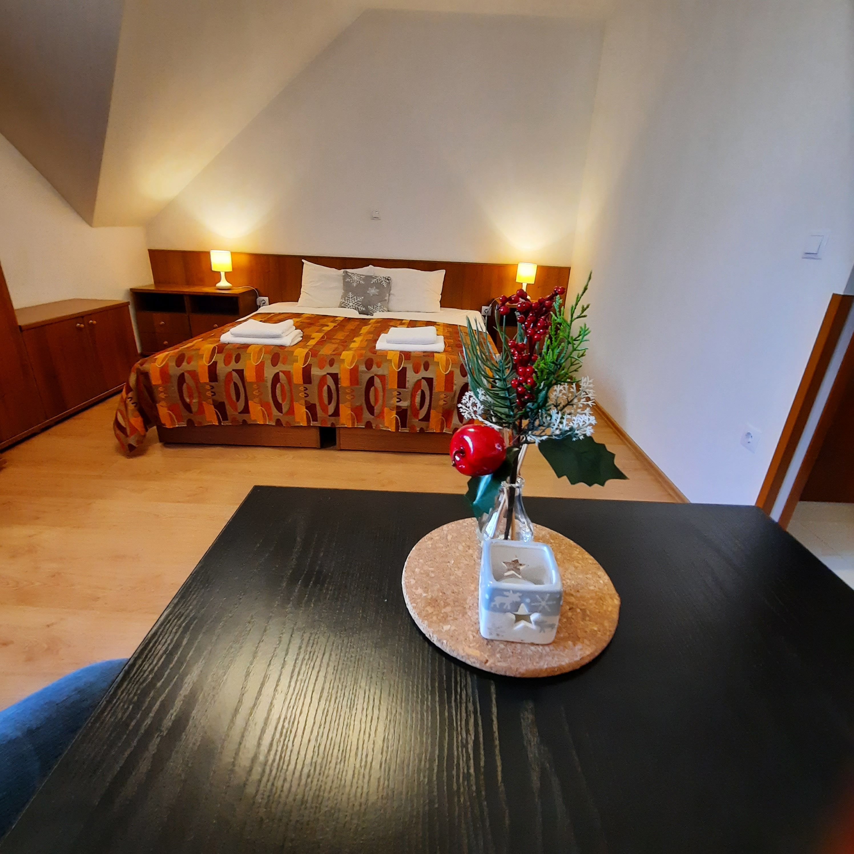 Hangulatos kétágyas szoba, előtérben egy díszített asztallal, háttérben egy ággyal.