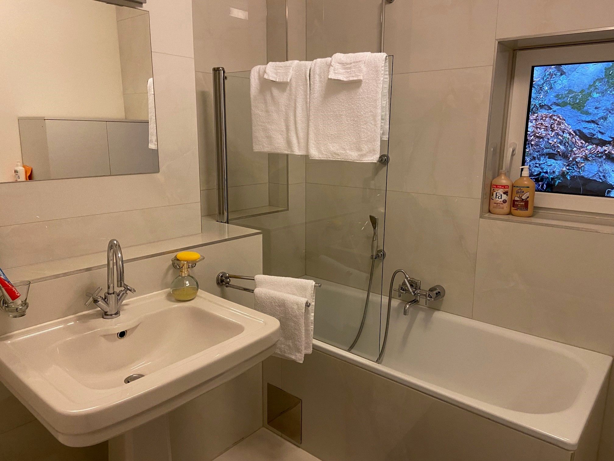 Modern fürdőszoba mosdóval, tükörrel, káddal és törölközőkkel.