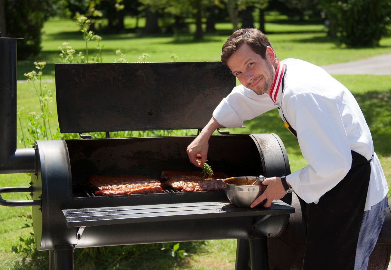 Egy szakács húst grillez egy nagy szabadtéri grillen.