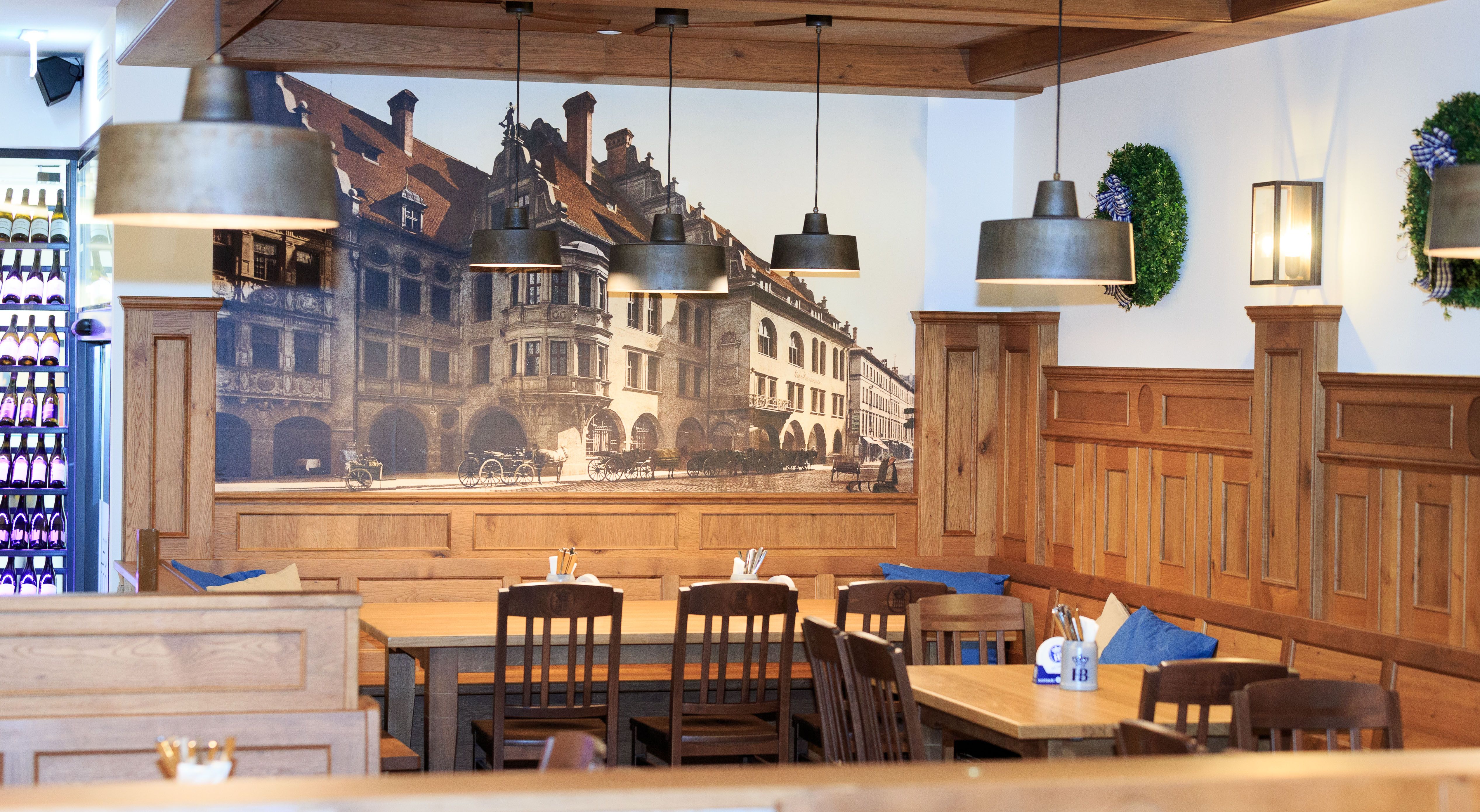 Egy hagyományos bajor étterem belső nézete, fa bútorokkal és a Hofbräuhaus falfestményével.