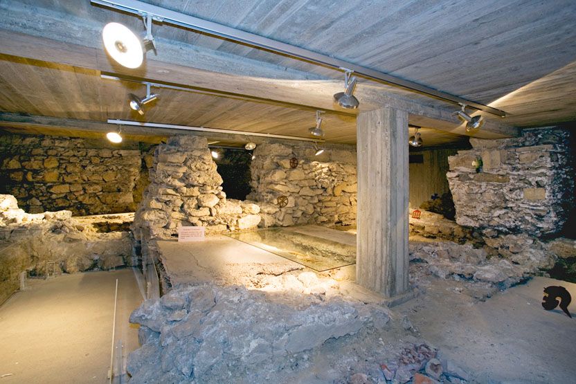 Földalatti romok kőfalakkal és betonoszlopokkal, mennyezeti spotlámpákkal megvilágítva.