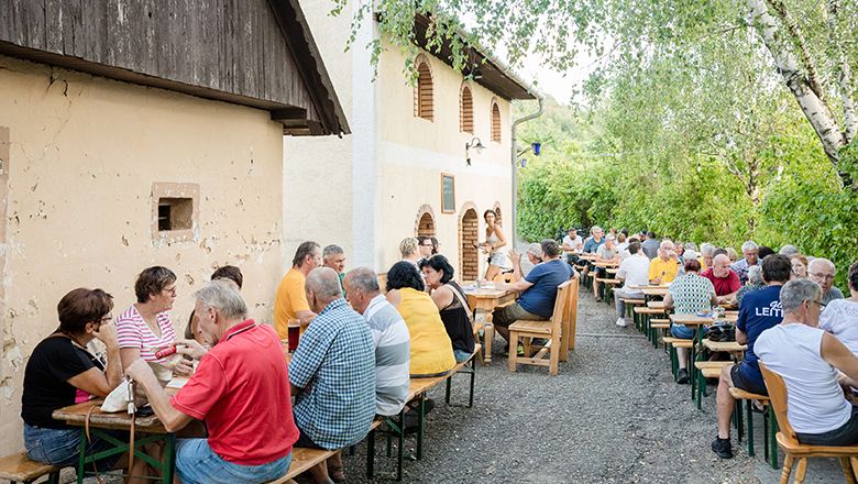 Az emberek hosszú asztaloknál ülnek kint egy hagyományos borozóban.