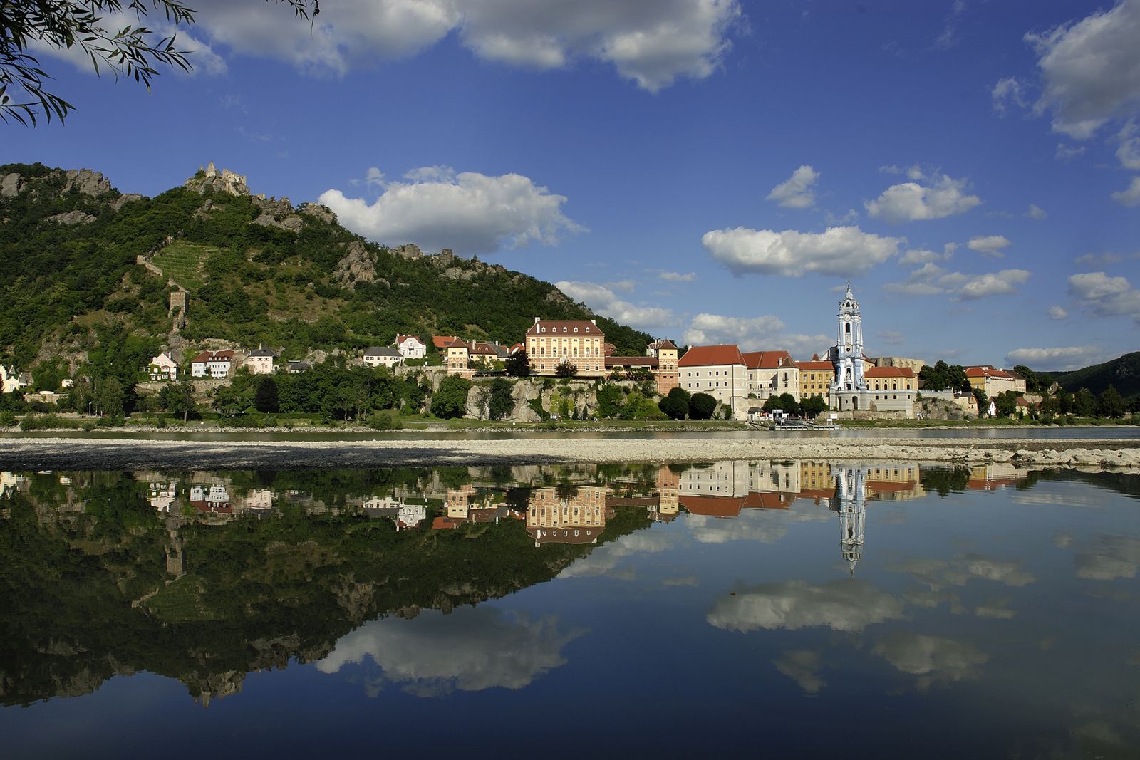 Dürnstein panorámája, előtérben a Duna, háttérben a várromok egy dombon.