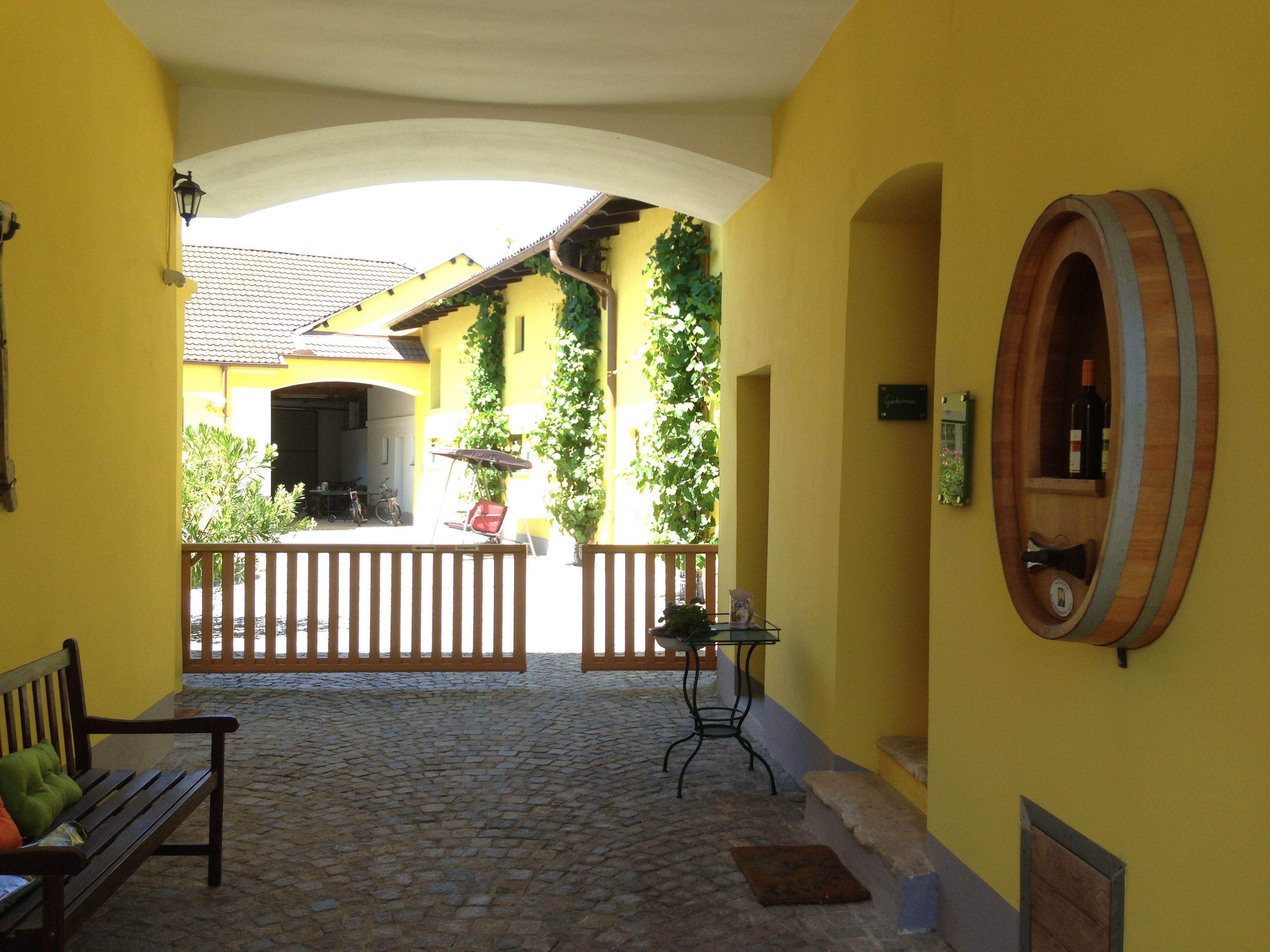 Sárga épület belső udvara boroshordós díszítéssel és fakapuval.