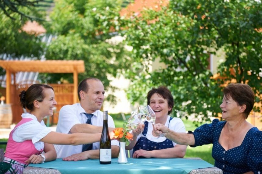 Négy ember koccint a borral egy kinti asztalnál.