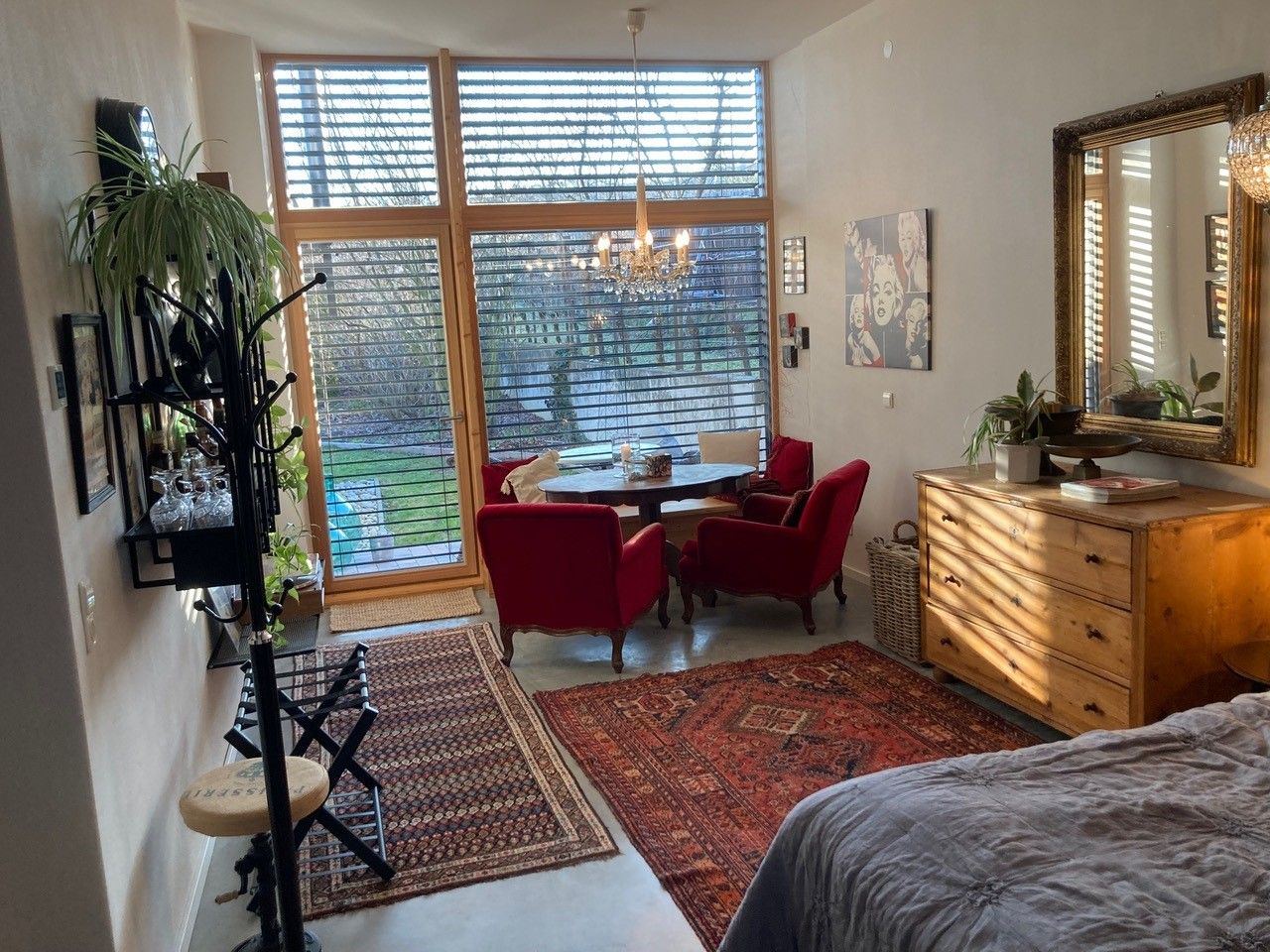 Nappali nagy ablakokkal, piros fotelekkel, fabútorokkal és szőnyegekkel, kilátással a kertre.