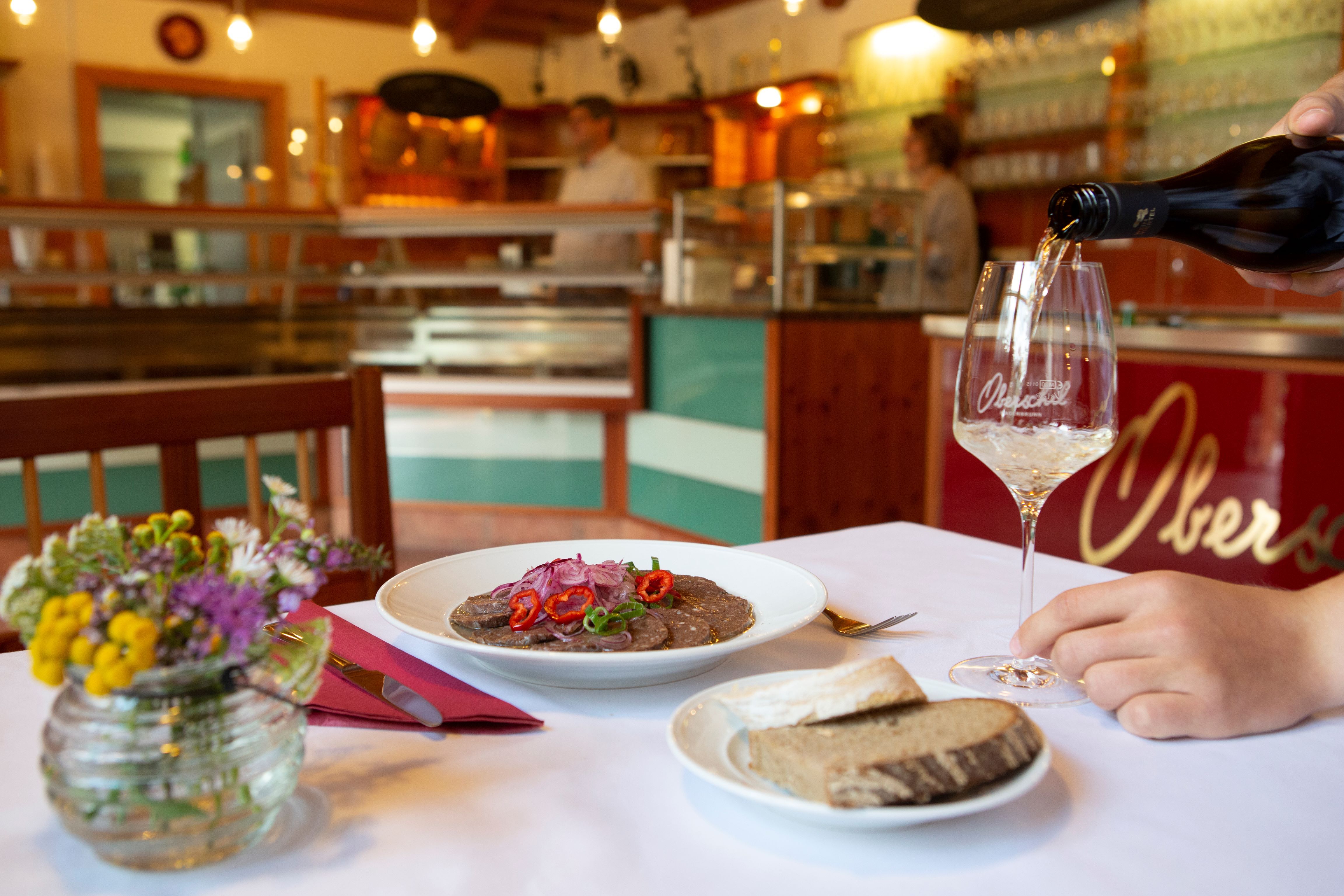 Megterített asztal egy borozóban, tál ételekkel, kenyérrel és egy pohár borral.