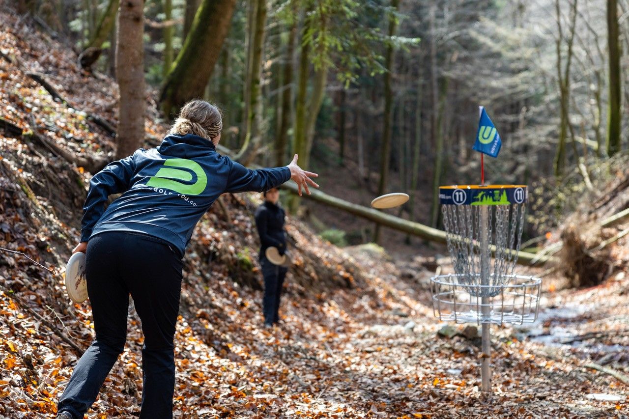 Egy személy frisbee-t dob az erdőben lévő disc golf kosárba.