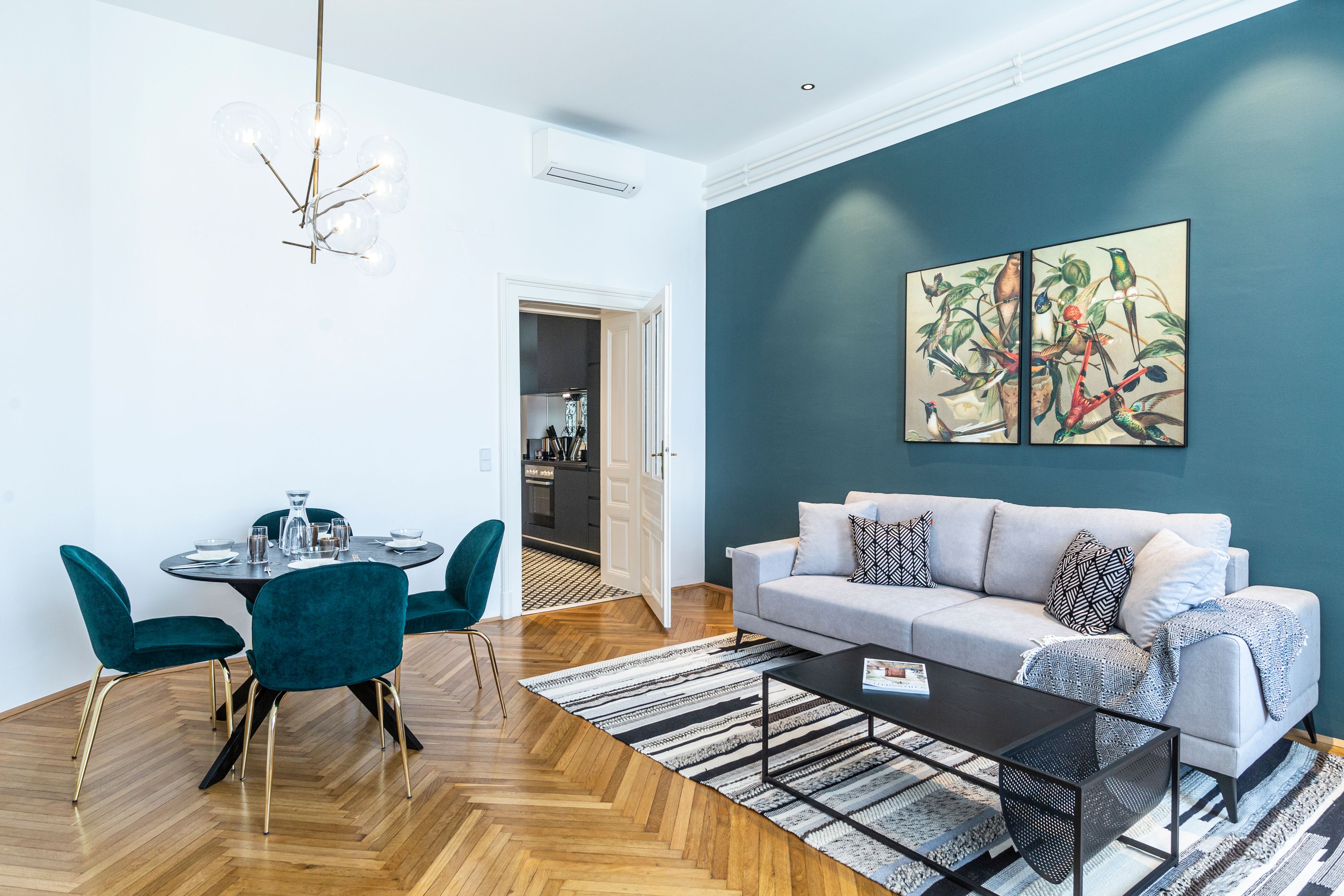 Modern nappali szürke kanapéval, étkezőasztallal és művészeti alkotásokkal a falon.