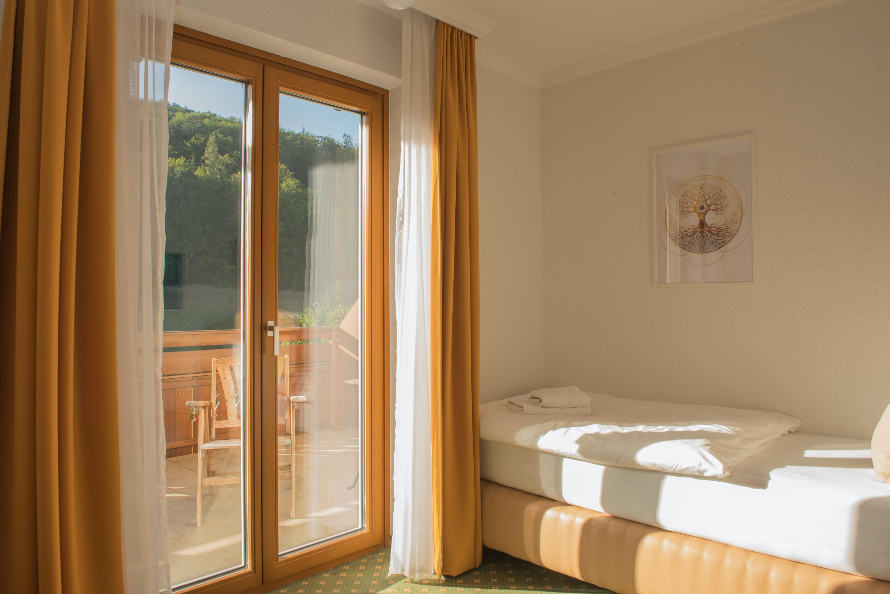 Egyágyas szoba erkéllyel, ágy, sárga függöny, fa erkély, napos.