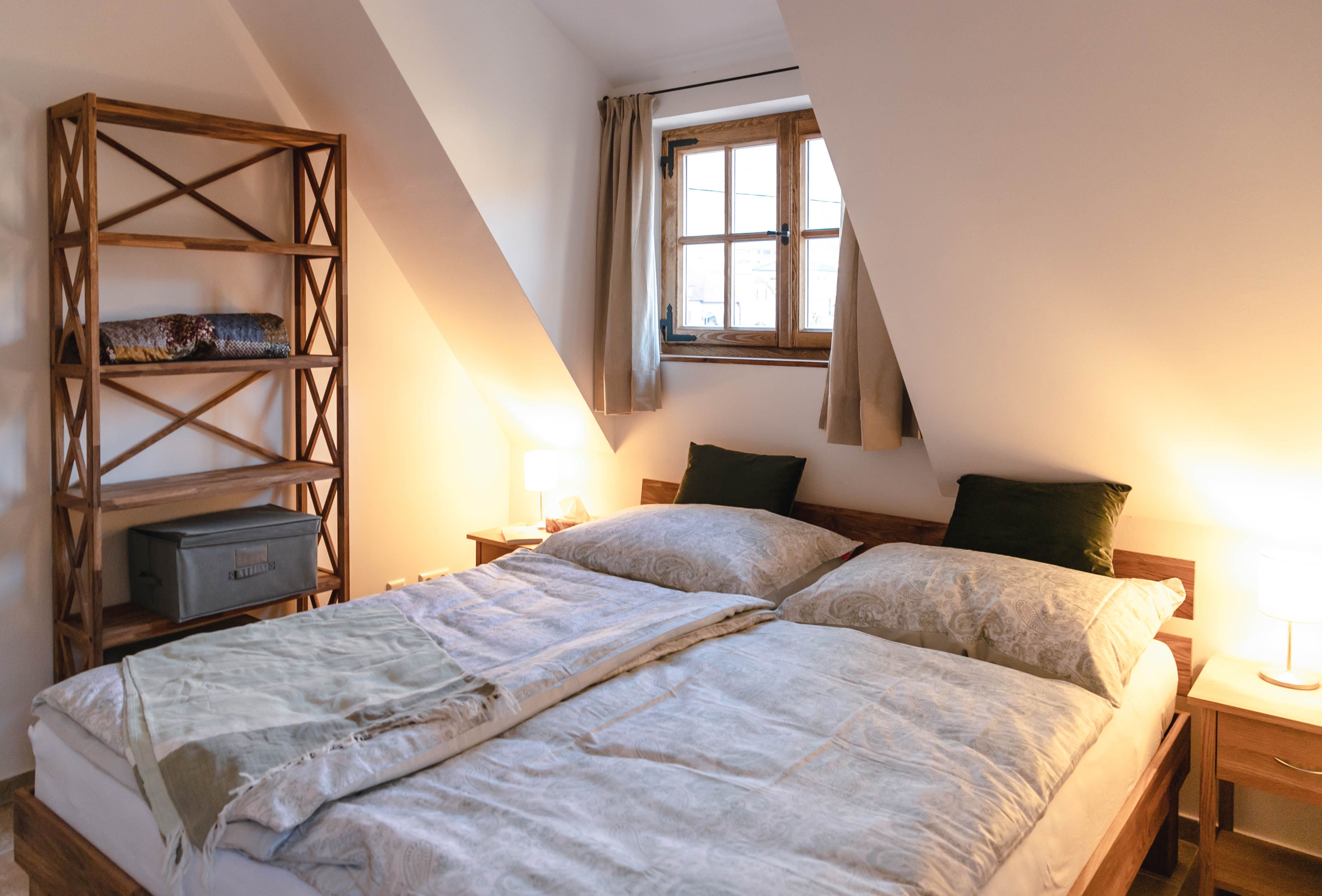 Hangulatos hálószoba franciaággyal, fából készült könyvespolccal és függönyös ablakkal.