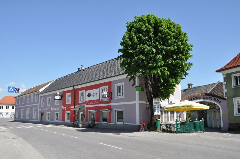Gasthof Wegl egy úton egy fával és napernyőkkel.