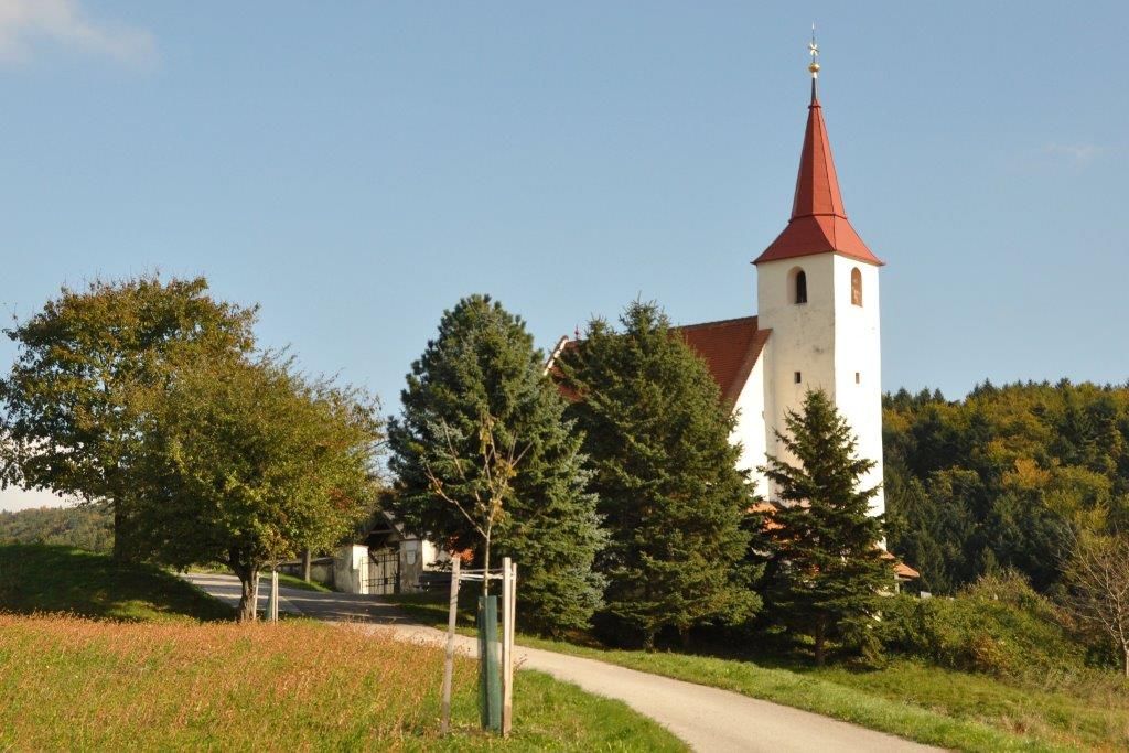 Ofenbach plébániatemplom piros toronytetővel, fákkal és rétekkel körülvéve.