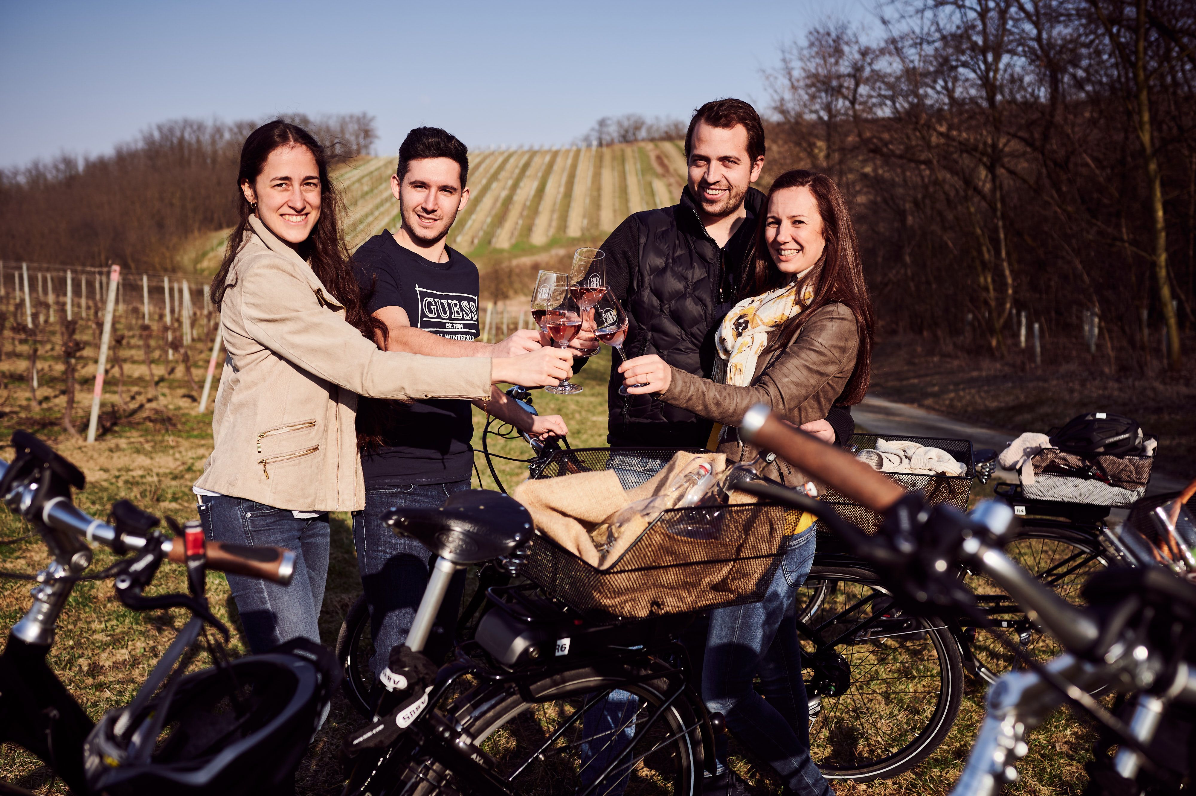 Négy ember koccint egy pohár borral, miközben e-bike mellett álldogálnak egy szőlőskertben.