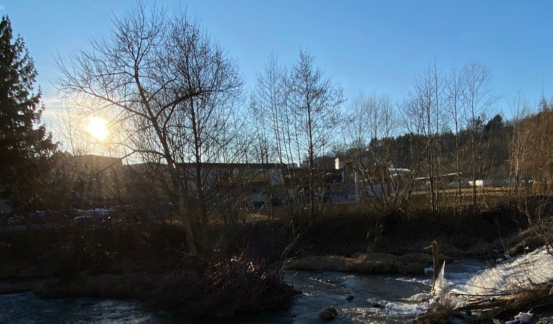 Naplemente a Zwettltal-völgyben a fák és a folyó mögött.