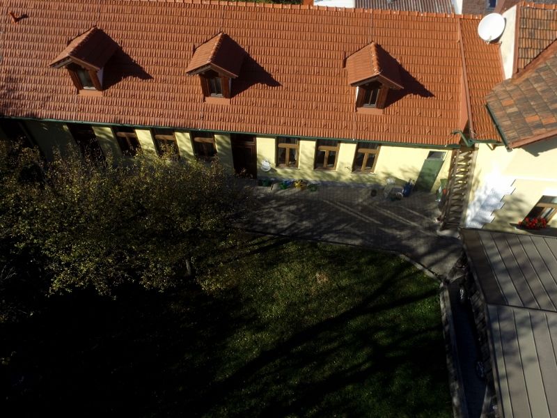 Légi felvétel egy piros cseréptetős, több ablakkal ellátott, kerttel körülvett épületről.