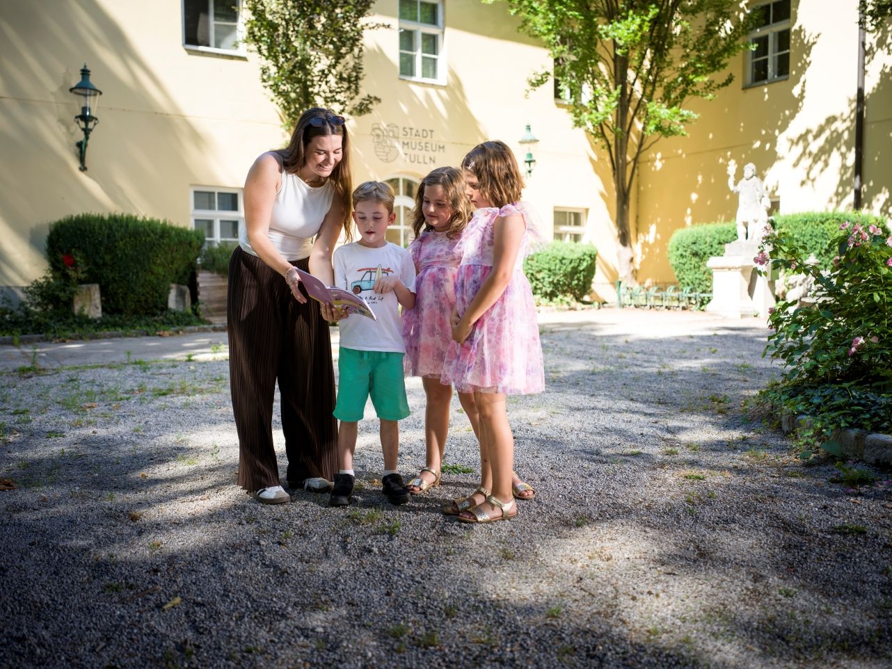 Egy nő és három gyermek áll a Tullni Városi Múzeum előtt, és a prospektust olvassák